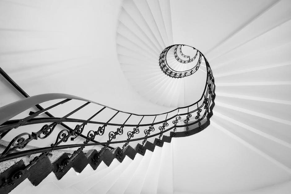 Black metal spiral staircase with artistic design in a white interior setting.