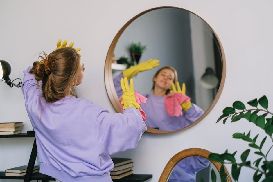 Back view of young female in casual clothes and latex gloves standing against mirror and dancing while cleaning light room in daytime